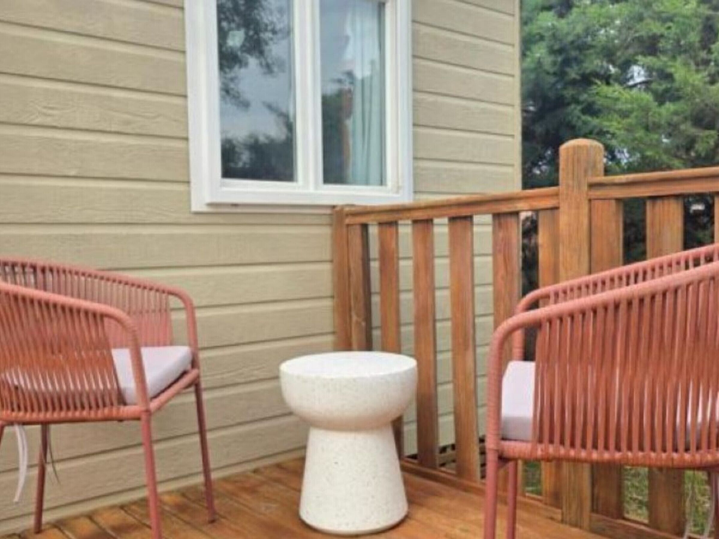 A wooden deck with two wicker chairs and a small white stool.