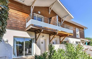 Een tweelaags huis met een balkon, grote schuifdeuren van glas en een houten gevel.