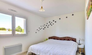 Een slaapkamer met een bed, een raam, een radiator, een plafondventilator en decoratieve wandversiering.