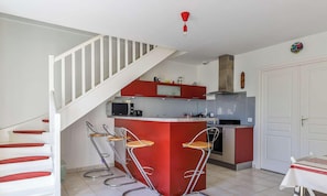 Een keuken met een rood kookeiland, een witte trap en een eetgedeelte met een tafel.
