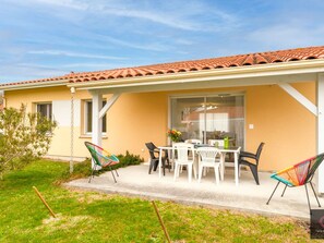Ein Haus mit einer Terrasse, einem Tisch und Stühlen sowie einem Garten.