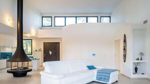 Una sala de estar moderna con un sofá blanco, una chimenea negra y una cocina al fondo.
