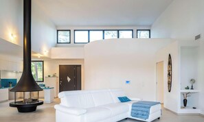 Ein modernes Wohnzimmer mit einem weißen Sofa, einem schwarzen Kamin und einer Küche im Hintergrund.