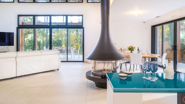 Una sala de estar moderna con un sofá, un comedor con una mesa y sillas, un ventanal grande y una lámpara colgante.