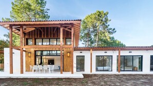 Una casa moderna de dos pisos con terraza de madera, ventanas grandes y fachada blanca.
