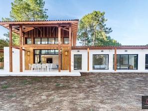 Ein modernes, zweistöckiges Haus mit einer Holzterrasse, großen Fenstern und einer weißen Fassade.