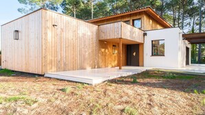 Una cabaña moderna de madera con un amplio balcón, una extensión blanca y un bosque de fondo.