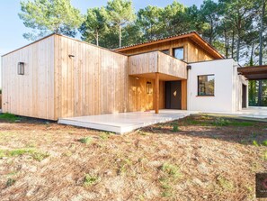 Eine moderne Holzjagdhaus mit einer großen Terrasse, einem weißen Anbau und Blick auf einen Wald.