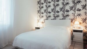 Una camera da letto con un letto, due comodini con lampade, una parete con motivo bamboo e una finestra con tende trasparenti.