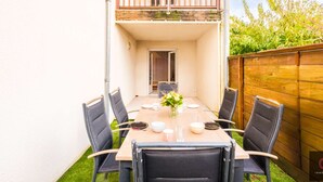 Un edificio a due piani con un balcone, un tavolo da pranzo con sedie e un piccolo giardino.