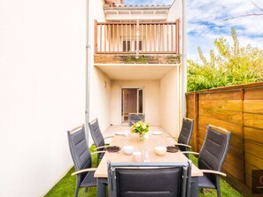 Ein zweistöckiges Gebäude mit einem Balkon, einem Esstisch mit Stühlen und einem kleinen Garten.
