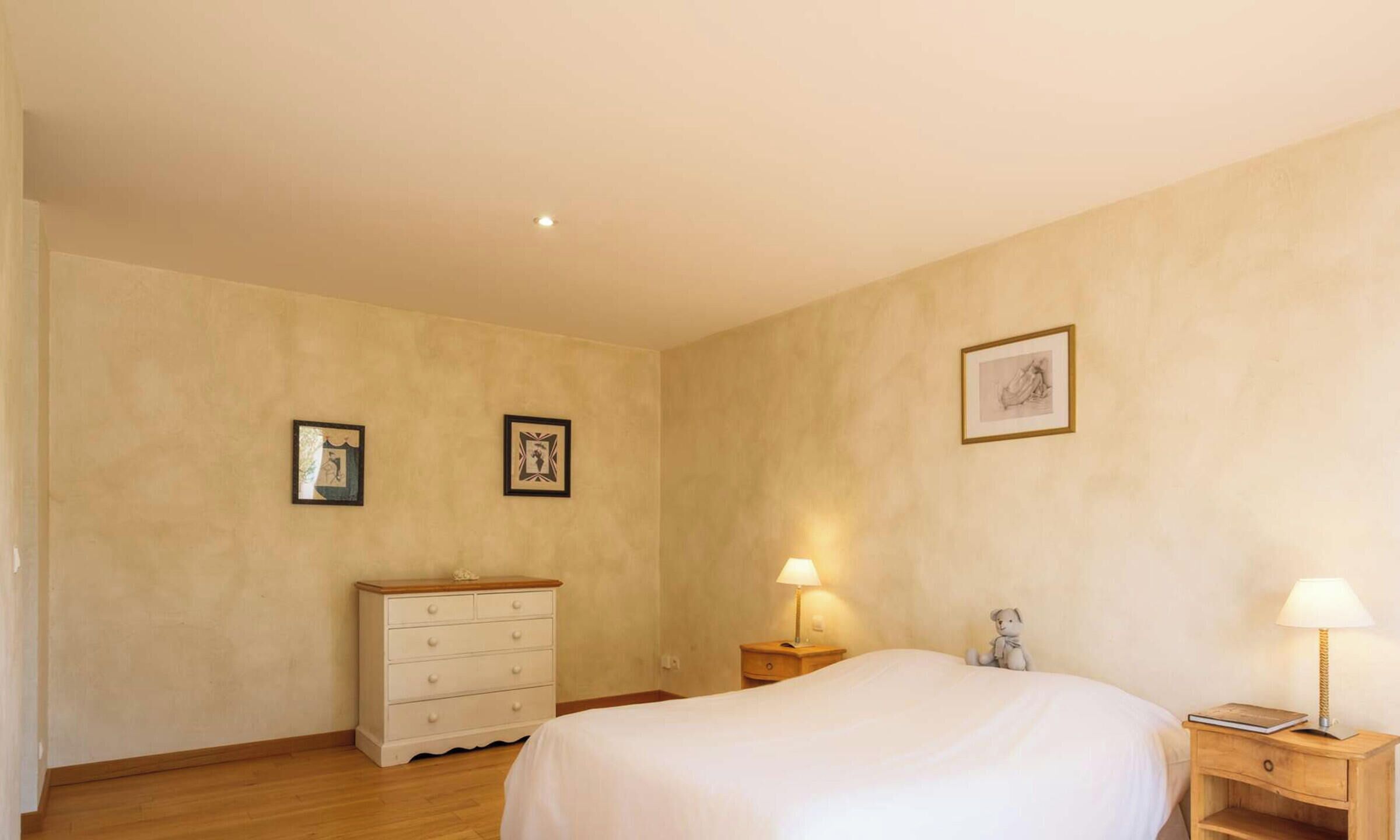 A bedroom with a bed, a dresser, two bedside tables with lamps, and two framed pictures on the wall.