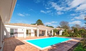 Ein Haus mit Schwimmbad, überdachter Terrasse und Garten.