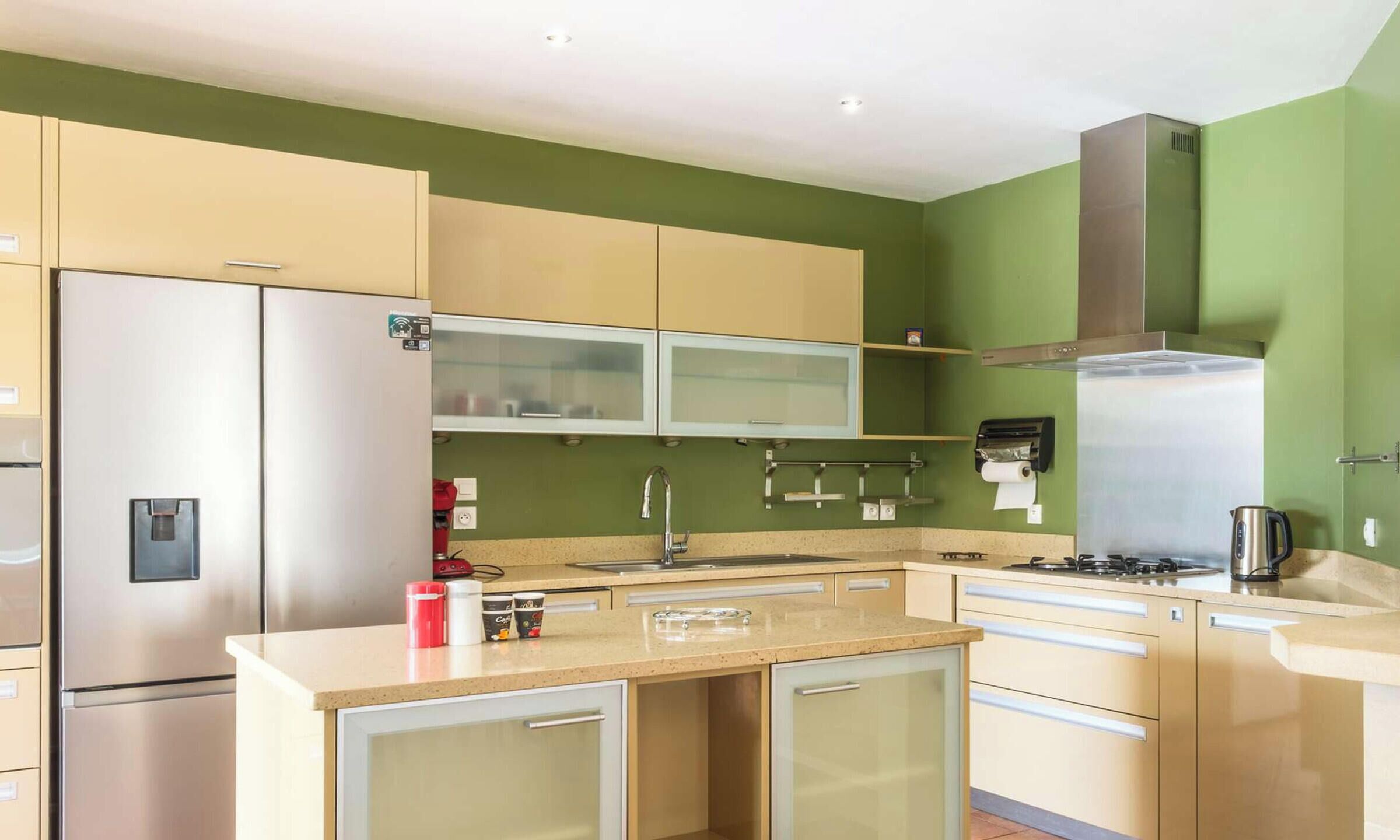 Une cuisine moderne dotée d’appareils électroménagers en acier inoxydable, d’un îlot central et de murs peints en vert.