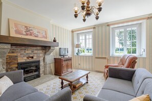 Un salon avec une cheminée, un canapé, un fauteuil en cuir, un téléviseur et un sol à motifs.