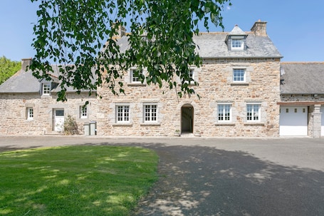 A stone building with a central entrance, multiple windows, and a paved driveway.. Holiday Home 'Gîte De L'Allégoat' with Private Garden