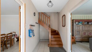 En trappe op til en etage, et spiseområde med stole og et bord, samt et skab med dekorative genstande.
