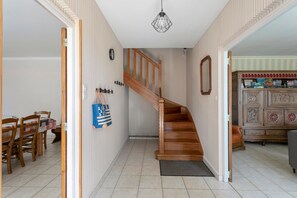 Een trap naar de tweede verdieping, een eethoek met stoelen en een tafel, en een kast met decoratieve objecten.