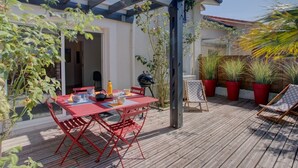 Un'area esterna con decking in legno, un tavolo e sedie rossi, un barbecue e piante in vaso.
