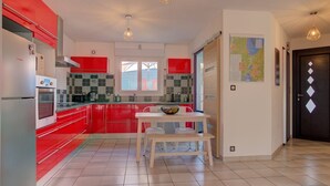 Una cucina moderna con mobili rossi, piani di lavoro bianchi e un'area pranzo con tavolo e panche.