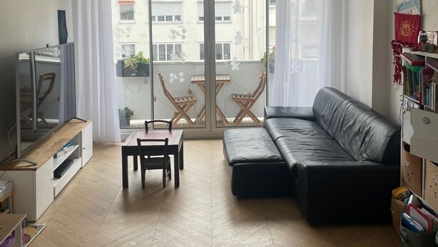 A living room with a sofa, a TV, a dining table with chairs, and a balcony with a view of buildings. - Apartment PARIS 1 MINUTE WALKING TO TOUR EIFFEL (Paris)
