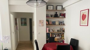 A dining area with a table, chairs, a hanging light fixture, and a bookshelf with various items. - Apartment PARIS 1 MINUTE WALKING TO TOUR EIFFEL (Paris)