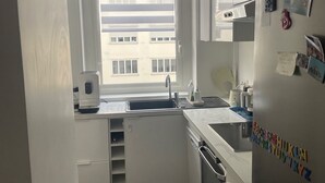 A compact kitchen with a built-in oven, a refrigerator with magnets, a window with blinds, and a ceiling fan. - Apartment PARIS 1 MINUTE WALKING TO TOUR EIFFEL (Paris)