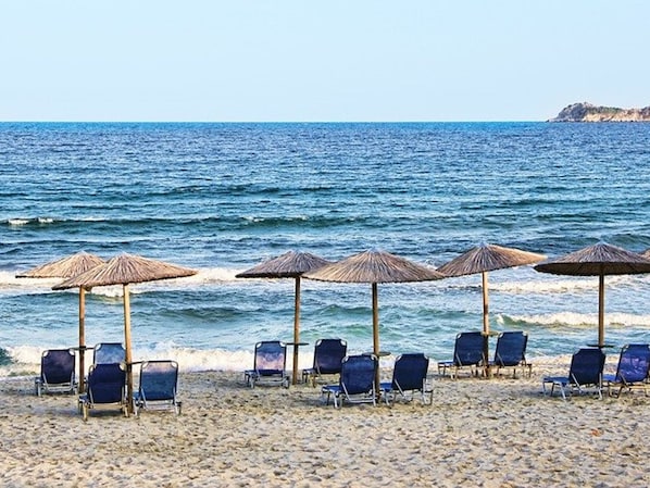 Ein Strand mit Liegestühlen und reetgedeckten Sonnenschirmen.