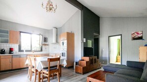 A modern kitchen with a dining area, a living room with a sofa, and a TV. - Charming wooden house near lake - 9 guests (Biscarrosse)