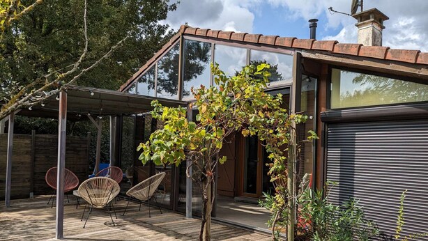 A modern house with a wooden deck, glass doors, and a pergola with chairs. - Charming wooden house near lake - 9 guests (Biscarrosse)