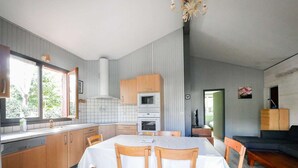 A modern kitchen with wooden cabinets, a dining table with chairs, and a built-in oven. - Charming wooden house near lake - 9 guests (Biscarrosse)