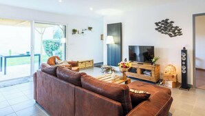 Ein modernes Wohnzimmer mit einem braunen Ledersofa, einem Fernseher, einem Holztisch und einer Glastür zu einem Außenbereich.