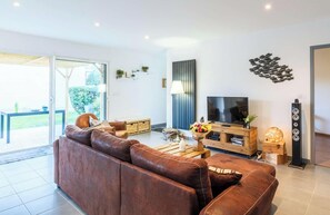 Ein modernes Wohnzimmer mit einem braunen Ledersofa, einem Fernseher, einem Holztisch und einer Glastür zu einem Außenbereich.