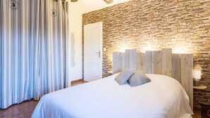 Ein Schlafzimmer mit einem Bett, einem Deckenventilator, einer Steinwand und einem Streifenvorhang.