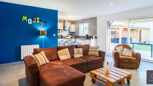 Ein modernes Wohnzimmer mit blauer Akzentwand, einem braunen Ledersofa, einem Holztisch und einer Küche im Hintergrund.