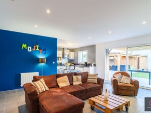Ein modernes Wohnzimmer mit blauer Akzentwand, einem braunen Ledersofa, einem Holztisch und einer Küche im Hintergrund.