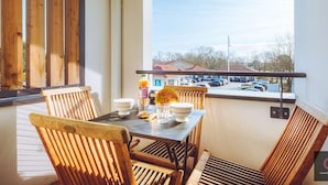 A balcony with a table and chairs, a view of a parking lot, and a building with a red roof. - Cozy apartment in the heart of Biscarrosse - 4 guests (Biscarrosse)