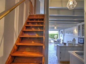 Eine Holztreppe führt zu einer Küche mit Essbereich und Ausblick ins Freie.