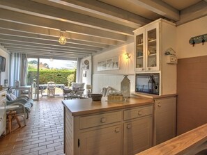 Eine Küche mit weißen Schränken, einer Holz Arbeitsplatte und einem Essbereich mit Korbmöbeln.