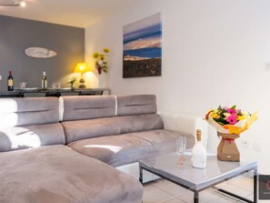 Ein modernes Wohnzimmer mit einem grauen Ecksofa, einem Glastisch und einem Blumenstrauß.