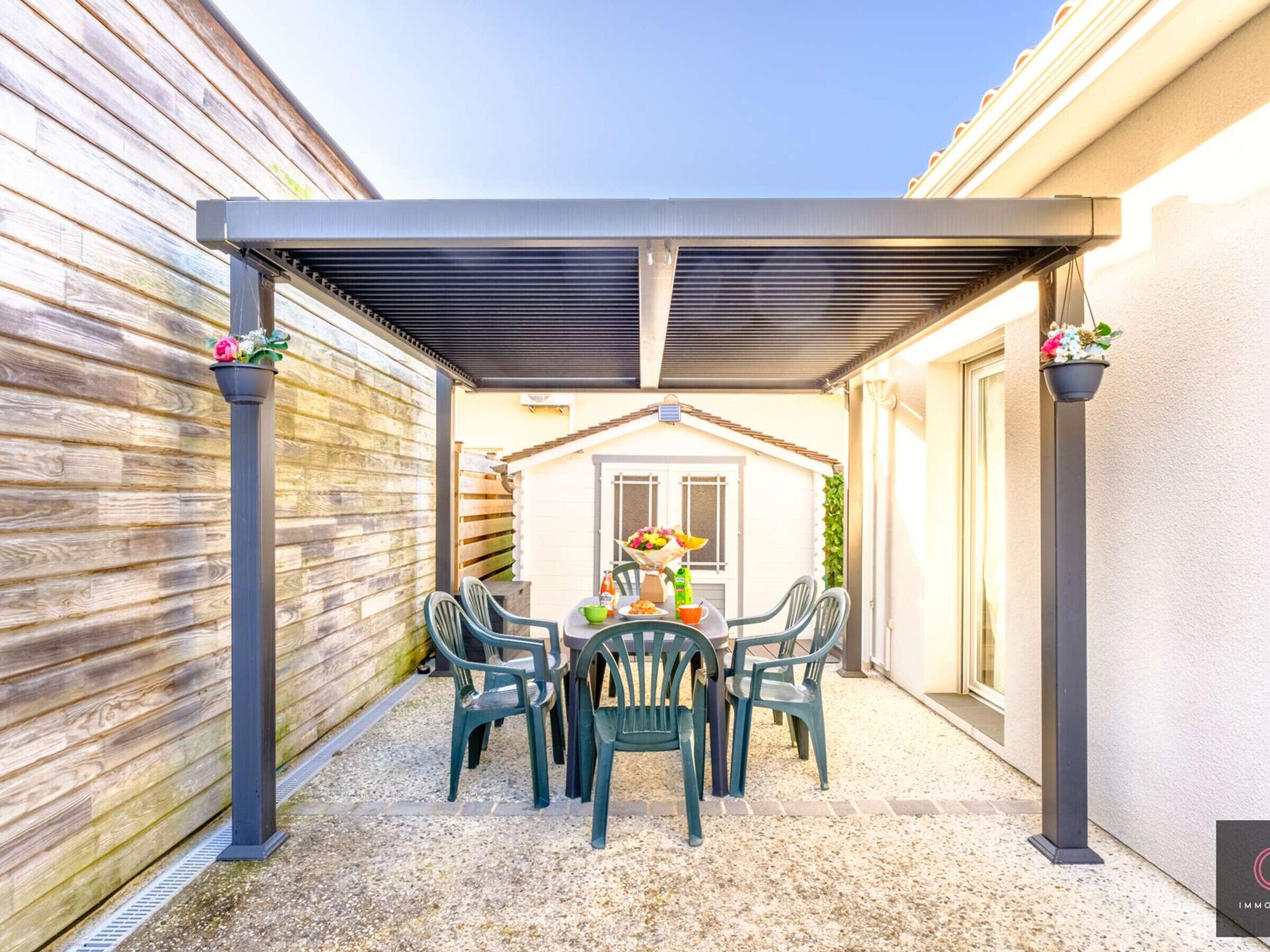 A covered patio with a table and chairs, a flower arrangement, and a house in the background.