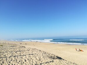 Ein Strand mit Sand, Wellen und blauem Himmel.