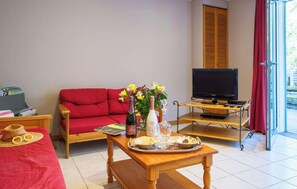 Ein Wohnzimmer mit einem roten Sofa, einem Holztisch mit Tablett, einem Fernseher auf einem Schrank und einem Fenster mit roten Vorhängen.