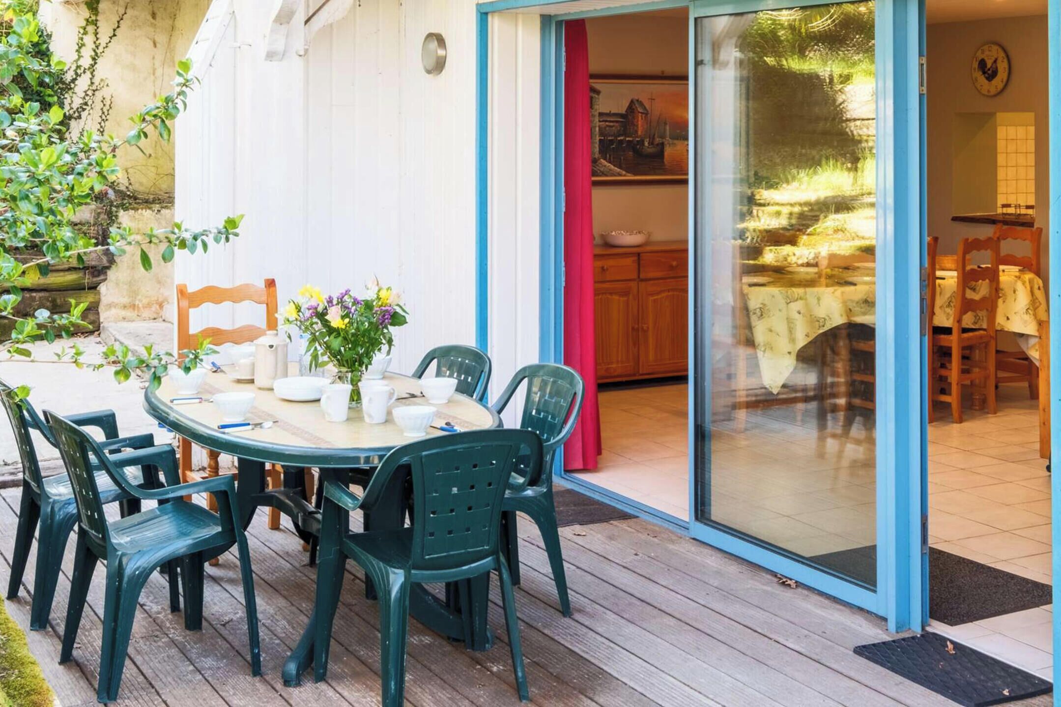 A patio with a round table and chairs, a sliding glass door leading to a kitchen, and a small garden area.