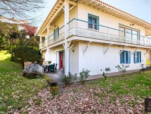 Ein zweistöckiges Haus mit Balkon, einer Terrasse mit Tisch und Stühlen sowie einem kleinen Garten.