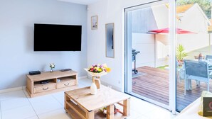 Ein modernes Wohnzimmer mit Flachbildfernseher, Holzmöbeln, einer Glastür zu einer Außenpatio und einer Blumenkomposition.