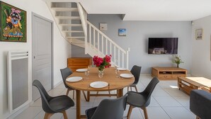 Ein Essbereich mit Holztisch, schwarzen Stühlen, einer Treppe, einem Fernseher und einem Bild an der Wand.