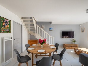Ein Essbereich mit Holztisch, schwarzen Stühlen, einer Treppe, einem Fernseher und einem Bild an der Wand.