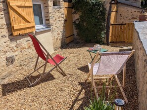 A stone building with a wooden door, a red folding chair, a table with a green tablecloth, and a solar-powered light post. - Studio with AC, peaceful village (Chenillé-Champteussé)