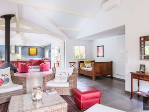 A spacious living area with a kitchen, red furniture, and a large window. - One-story villa with pool - 8 guests (Biscarrosse)